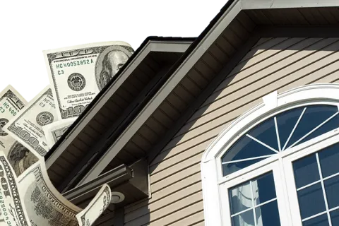 Close-up of house exterior with window and hundred-dollar bills flying behind the roof.