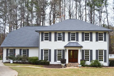 Elegant white home with black shutters surrounded by trees and well-maintained landscaping.
