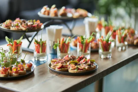 Assorted colorful appetizers and vegetable cups arranged on a wooden table for a catered event or party.