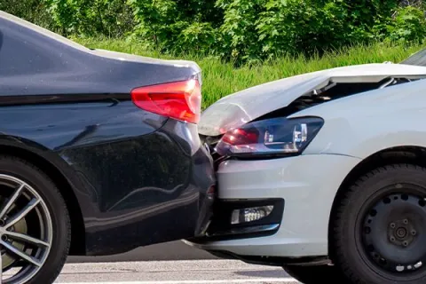 Rear-end collision between a white car and a black car on a sunny day with trees in the background.