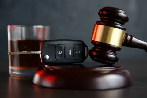 Car key, judge gavel, and a glass of dark liquid representing DUI and legal consequences.