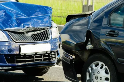 Blue and black cars with severe front-end damage after a collision on a road.