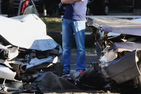 Two cars with severe front-end damage after a collision, person standing nearby assessing the crash scene
