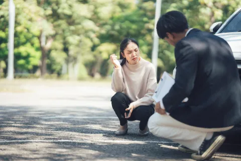 Woman and man crouching by a car examining damage during an insurance claim inspection outdoors