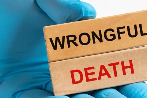 Hand in blue glove holding wooden blocks with the words Wrongful Death against white background