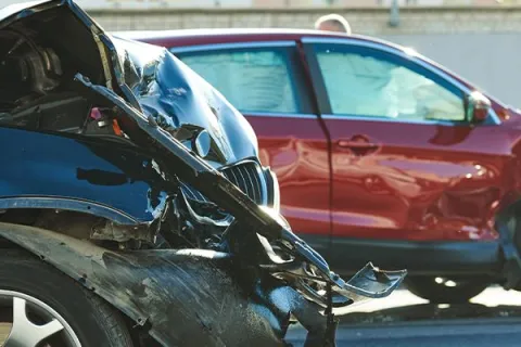 Front-end damage on a blue and a red car after a collision in a parking area on a sunny day