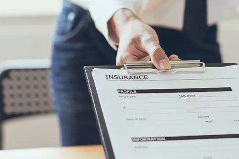 Person holding an insurance application form on a clipboard ready for signing at a desk.