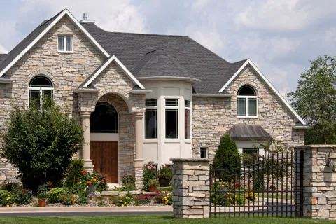 Elegant stone house with a landscaped garden and decorative gate under a bright sky.