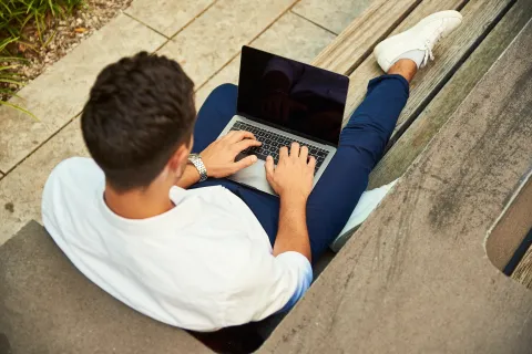 a man sitting on a bench using a laptop