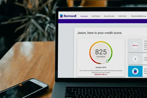 Laptop screen displays Borrowell credit score dashboard showing an excellent 825 score and a smartphone on wooden table