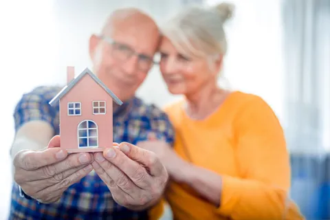 Senior couple holding a small model house symbolizing home ownership and retirement planning.