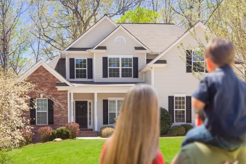 Family enjoying a sunny day in front of a beautiful suburban home with lush greenery.
