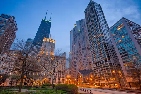 Chicago skyline at dusk with illuminated skyscrapers and leafless trees in foreground city park