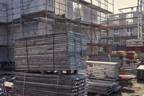 Construction site with scaffolding, building materials, and machinery on a sunny day.