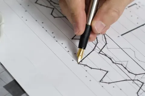 Close-up of a hand holding a pen over a financial graph with a coffee cup nearby.