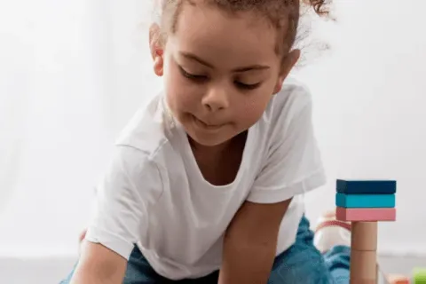 Young girl engaged in playful activities with colorful building blocks on the floor.