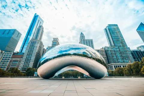 Cloud Gate sculpture reflecting Chicago skyline on a sunny day, surrounded by modern buildings.