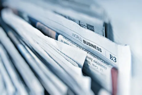 Close-up of stacked newspapers showcasing world business headlines and articles.