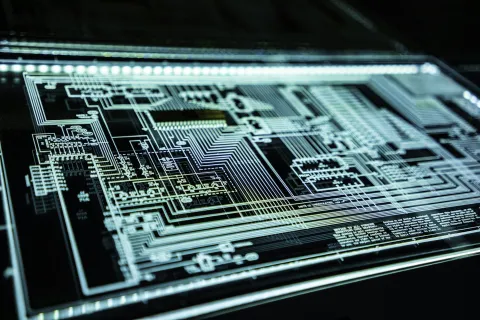 Close-up of a black circuit board with intricate silver circuitry details illuminated by LED lights.