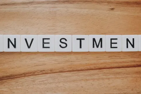 White letter tiles spelling INVESTMENT on a wooden surface representing finance and business concepts.