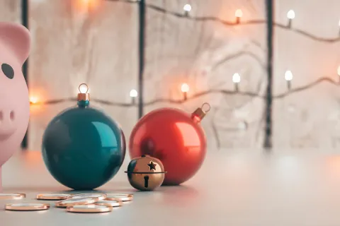 Pink piggy bank with coins, holiday ornaments, and string lights on a wooden surface festive saving concept