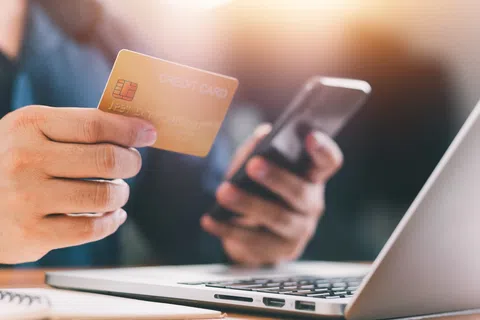 Person holding a credit card and smartphone making an online payment with a laptop in view.