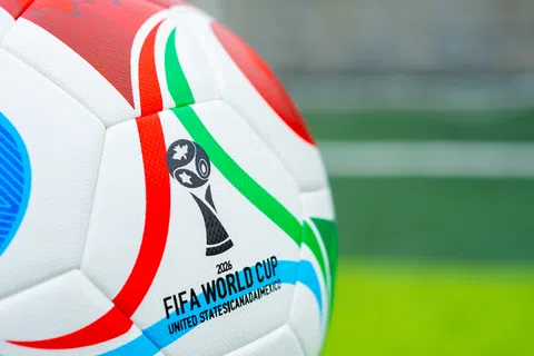 Close-up of the 2026 FIFA World Cup official soccer ball with colorful red, green, and blue stripes on a green field.