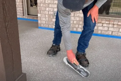Worker applying coating on concrete garage floor near brick wall and window