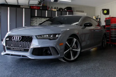 Gray Audi Quattro parked in a clean garage with red tool cabinets and white walls under bright lighting.