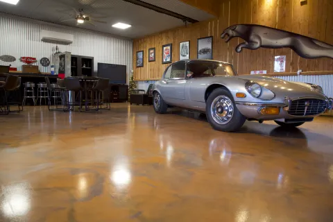 Silver classic Jaguar E-Type car in a stylish garage with wooden walls and bar seating area