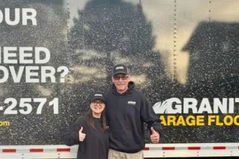Two people in black hoodies and caps giving thumbs up standing in front of a Granite Garage Flooring truck.