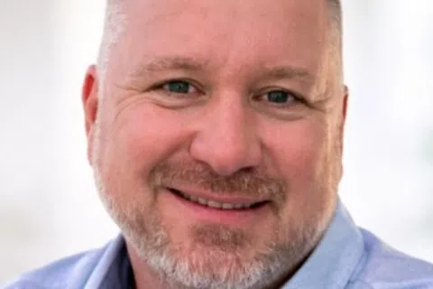 Smiling man with short hair and beard under Granite Garage Floors logo on neutral background.