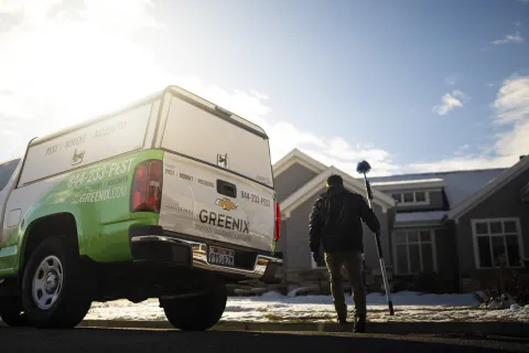 Greenix pest control truck parked outside a house with technician walking towards home holding equipment in winter.