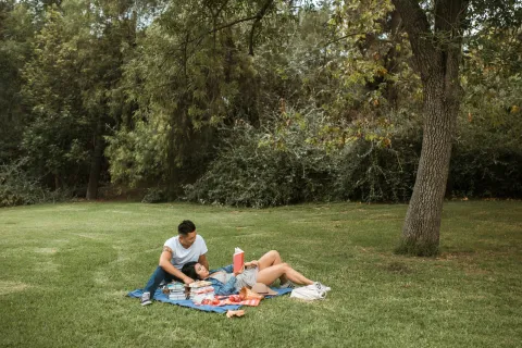 a man and woman sitting on a blanket in a grassy area
