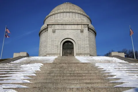 a stone building with a dome and flags on the top with McKinley National Memorial in the background