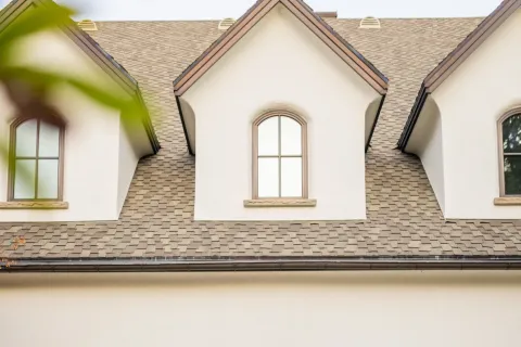 Worker cleaning exterior wall light fixtures on a beige house with three dark garage doors and arched windows.