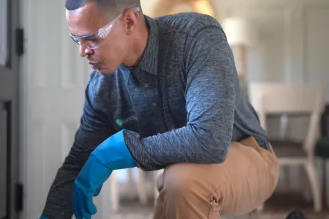 Man wearing protective gloves and safety glasses inspecting a door frame in a home interior.