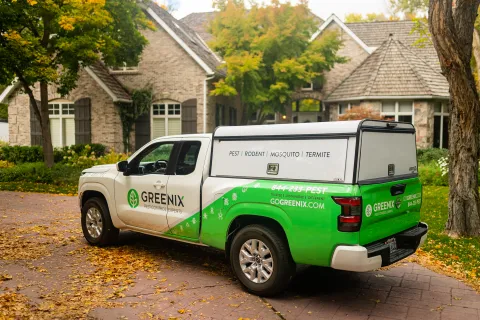 Greenix pest control truck parked in a residential driveway during autumn with home and trees in background.