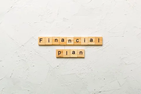 Wooden letter blocks spelling out "Financial Plan" on a white textured background, highlighting effective financial planning and physician burnout solutions.