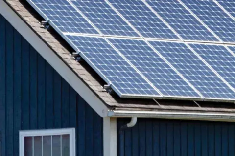 Solar panels installed on the roof of a blue house under clear daylight.