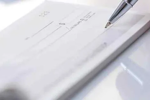 Close-up of a pen poised to write on a blank checkbook with financial details visible.