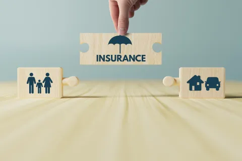 Hand placing insurance puzzle piece connecting family and home car insurance icons on wooden surface
