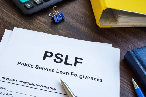 Public Service Loan Forgiveness (PSLF) form with pen, calculator, and office supplies on wooden desk.