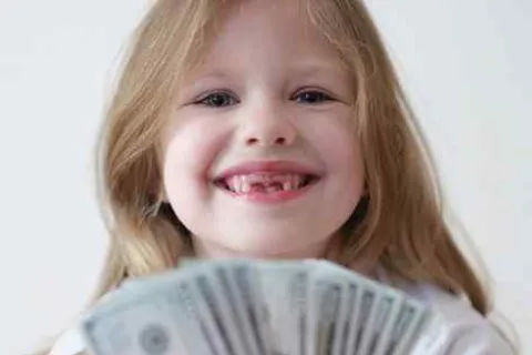 Smiling young girl with missing front teeth holding fanned US dollar bills showing joy and excitement.