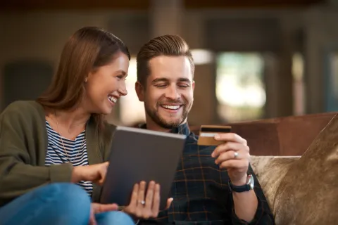 Happy couple shopping online with tablet and credit card while sitting on a couch at home