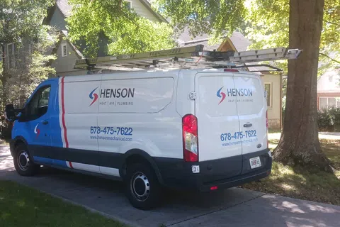 Henson heating and plumbing service van parked on a residential driveway with trees and houses in the background