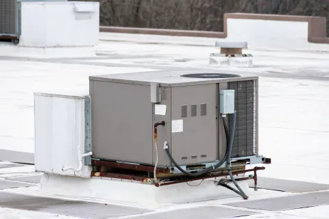 Commercial HVAC unit installed on a flat rooftop with electrical and piping connections visible.
