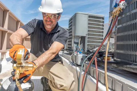 HVAC technician in safety gear working on air conditioning units on rooftop under clear sky