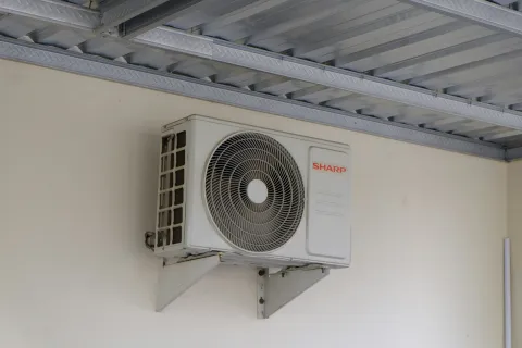 White Sharp brand air conditioning outdoor unit mounted on a wall under a metal roof.