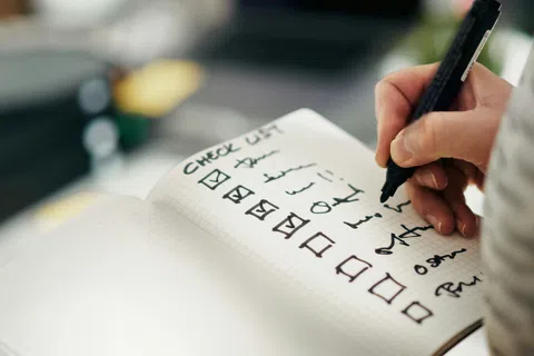 Hand writing on a checklist notebook with multiple items checked and some unchecked in black ink.
